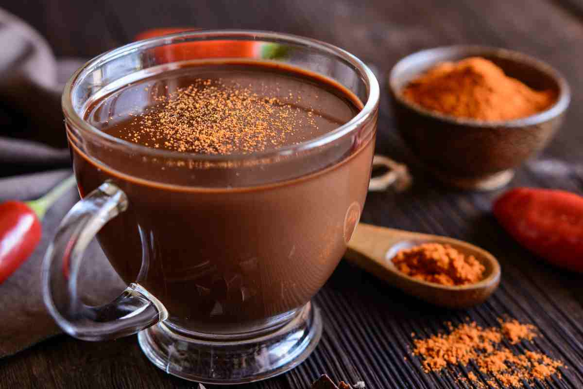 Cioccolata calda al peperoncino in una tazza vicino a una ciotola con polvere di peperoncino secco e peperoncini freschi