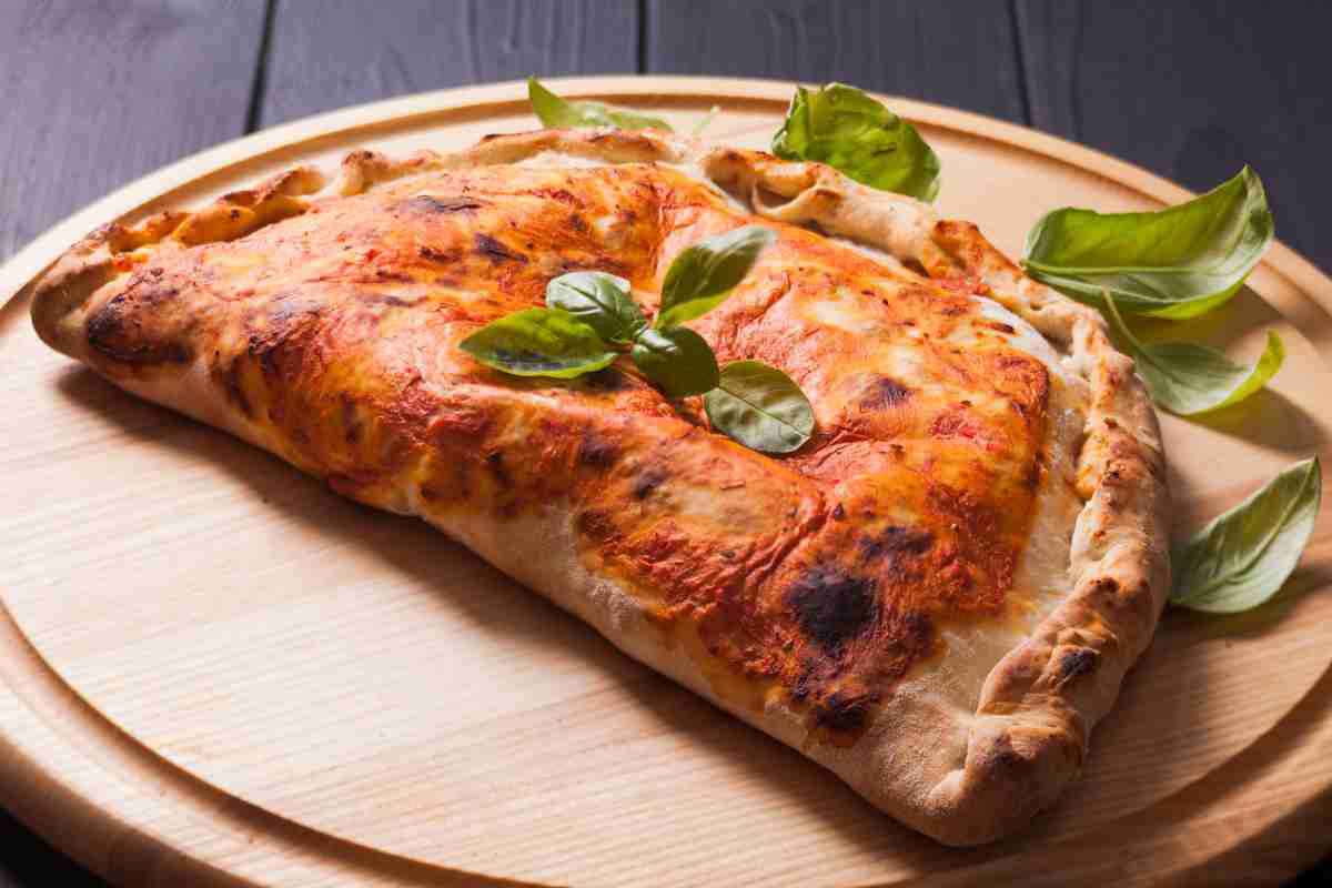 Calzone farcito ricotta e prosciutto sul tagliere di legno rotondo