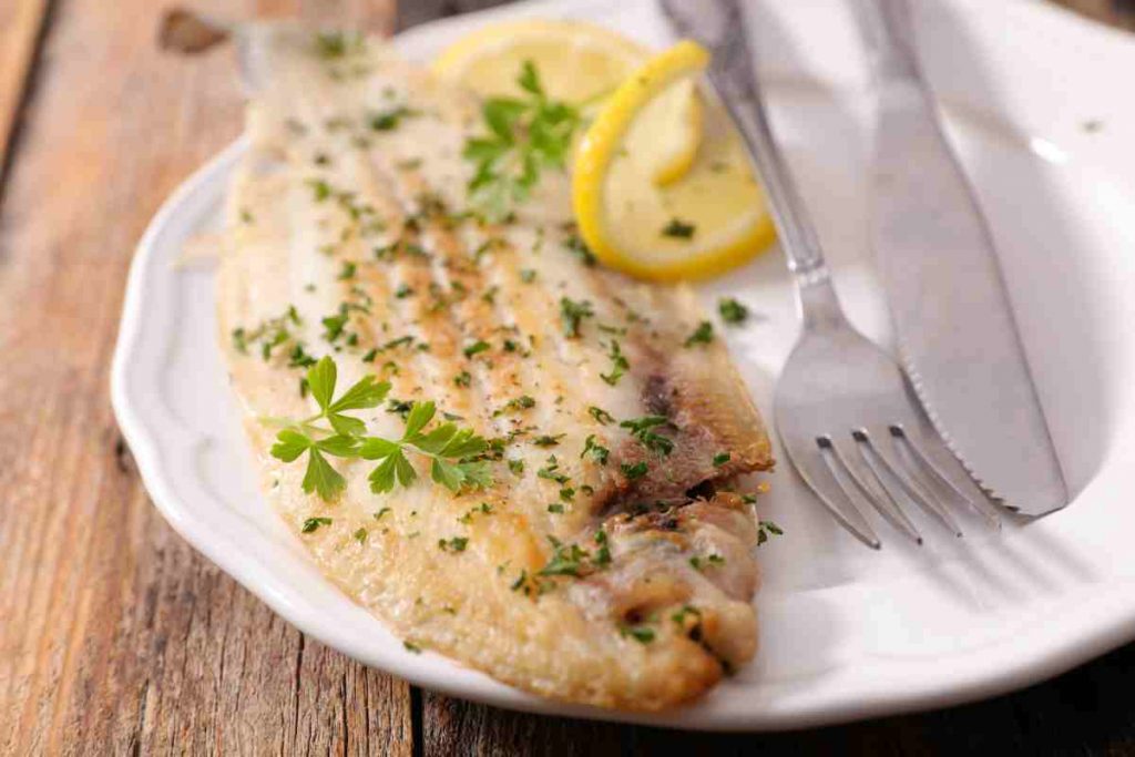 Sogliola al limone al forno con spicchi di agrume e prezzemolo in un piatto 