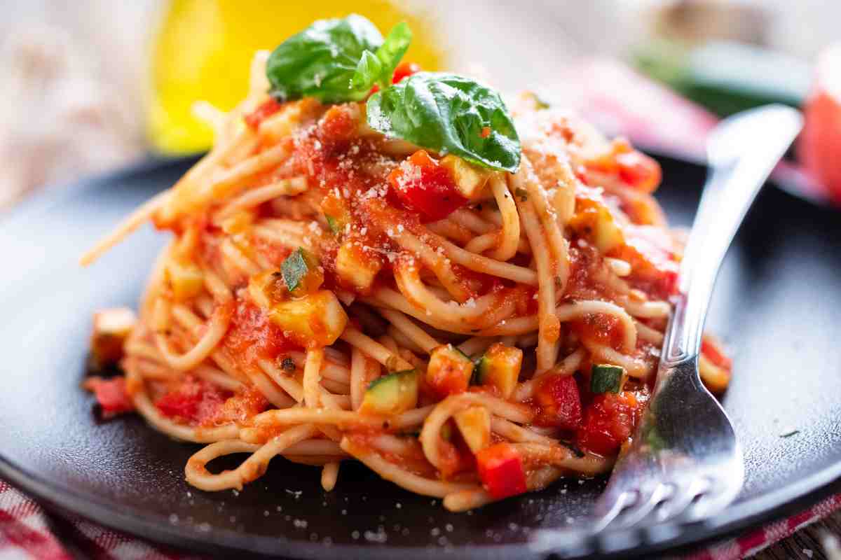 Pasta speck zucchine e pomodoro in un piatto nero