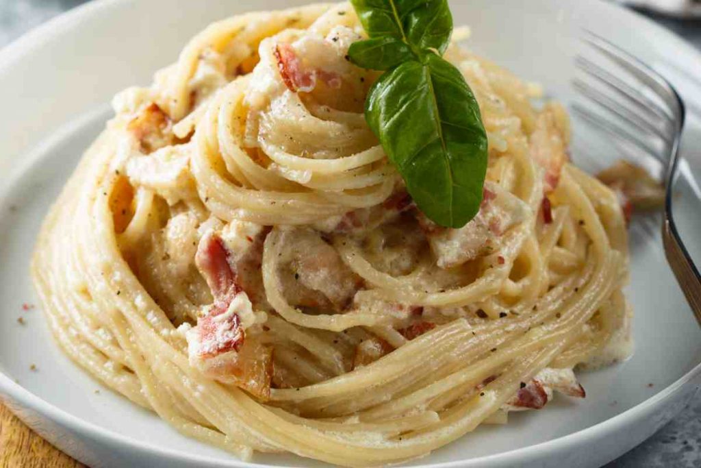 Pasta alla gricia arrotolata in un piatto con foglie di basilico sopra