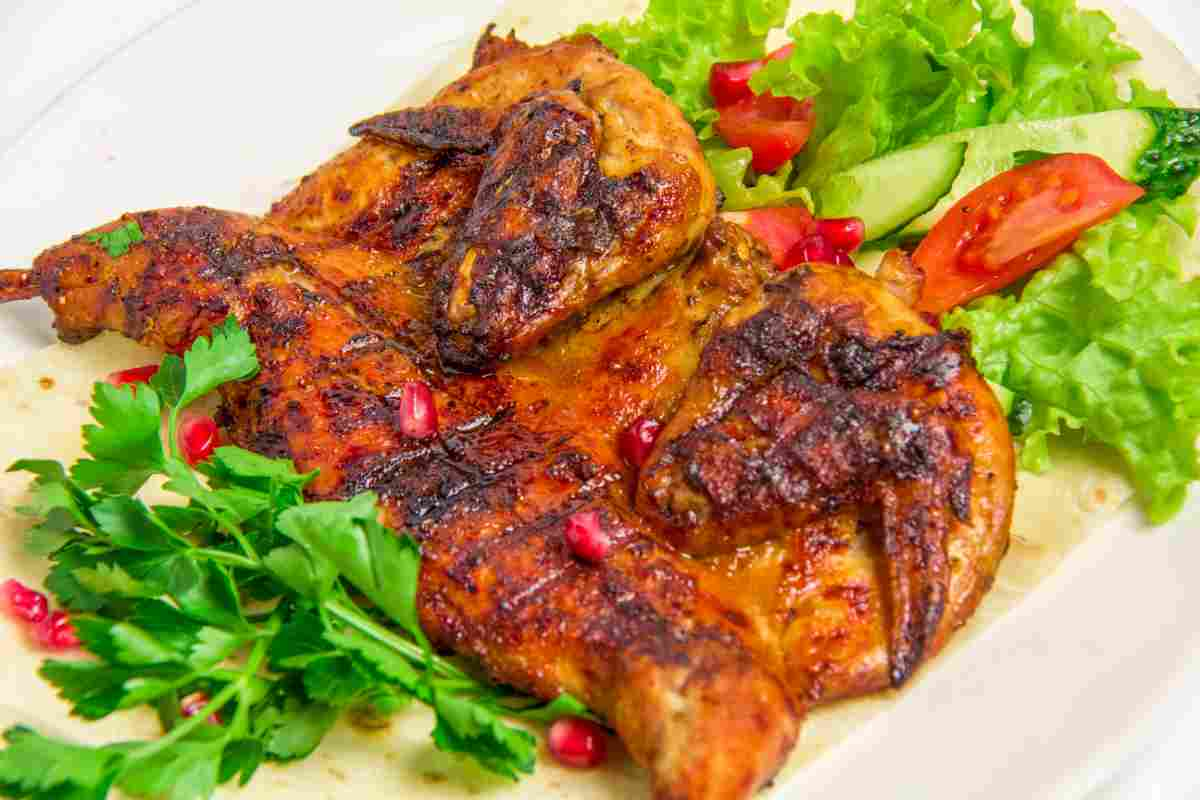 Pollo alla griglia in un piatto con insalata verde e melograno