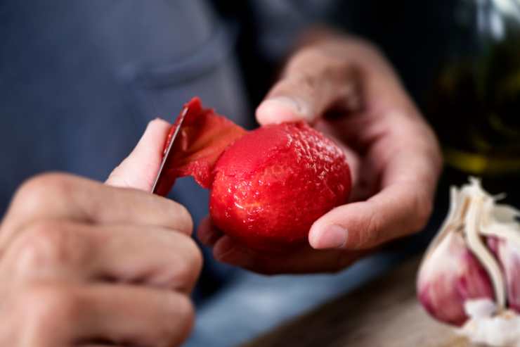 Un uomo che sbuccia un pomodoro sbollentato