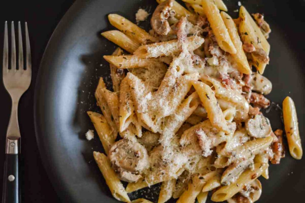 Pennette alla boscaiola in bianco con panna su un piatto nero