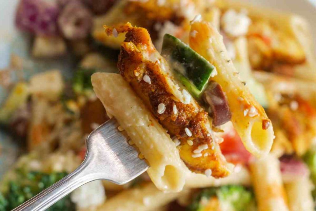 Pasta fredda con verdure, carne e formaggio guarnita con semi di sesamo