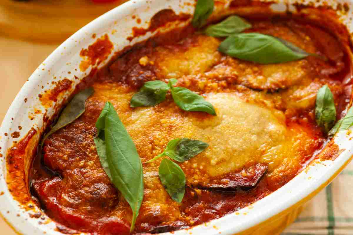 Parmigiana di melanzane guarnita con foglie di basilico in una pirofila ovale bianca