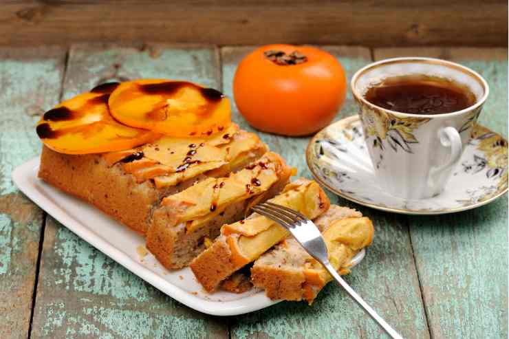 Torta ai cachi di forma rettangolare tagliata a fette su un vassoio con una tazza di tè