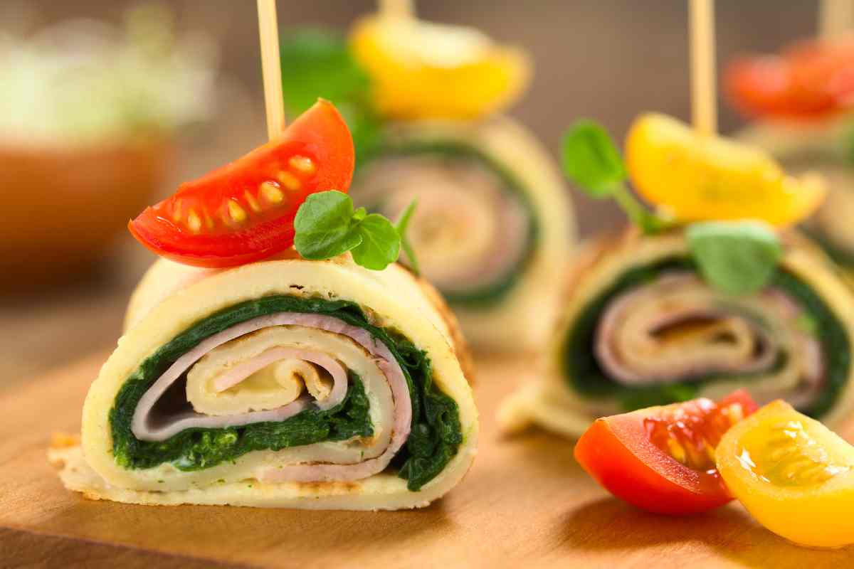 Crepes salate ripiene di spinaci e prosciutto tagliate a rotolini per la ricetta del giorno