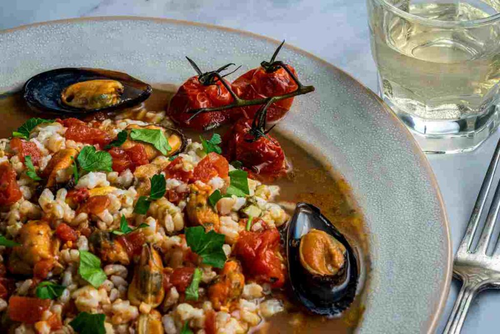 Orzo e cozze in un piatto fondo con vicino un bicchiere di vino