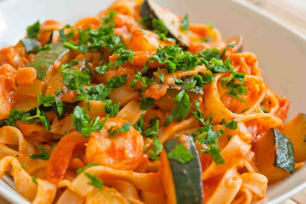 Tagliatelle con gamberi e zucchine cosparse di prezzemolo su un piatto bianco