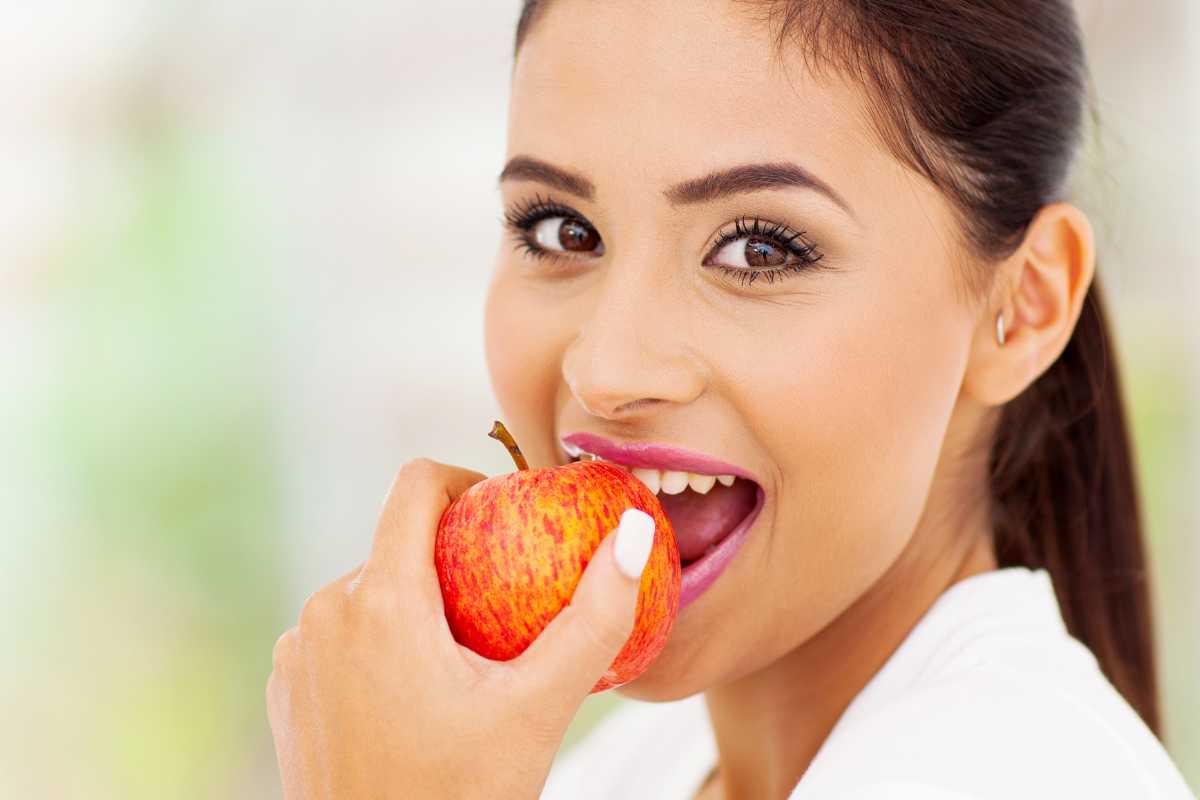 donna porta una mela alla bocca come esempio di cosa mangiare per prevenire le rughe