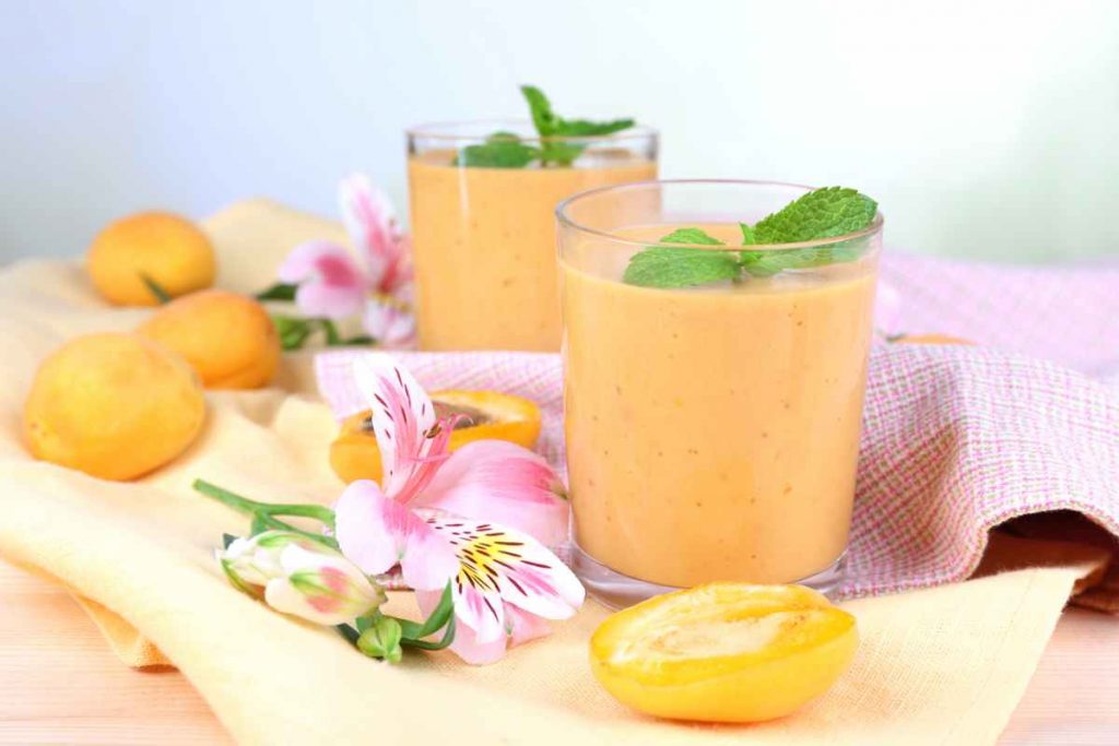 Due bicchieri pieni di fruttolo alle albicocche fatto in casa con frutta sul tavolo e fiori