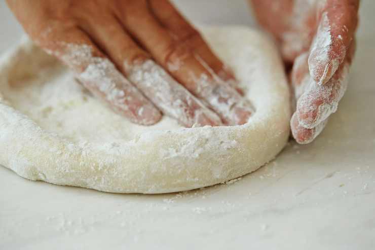 mani che lavorano l'impasto per la pizza stracciatella zucchine e alici