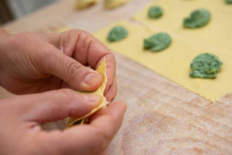 Mano che chiude i pansotti liguri con le erbe 