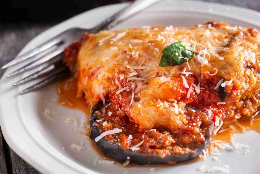 Parmigiana di melanzane in padella con mozzarella in un piatto bianco con vicino la forchetta