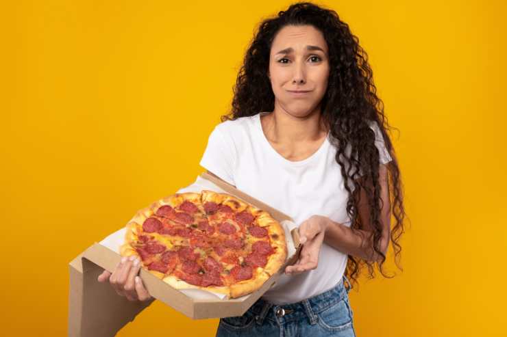 Ragazza con una pizza al salame triste perché soffre di cattiva digestione 