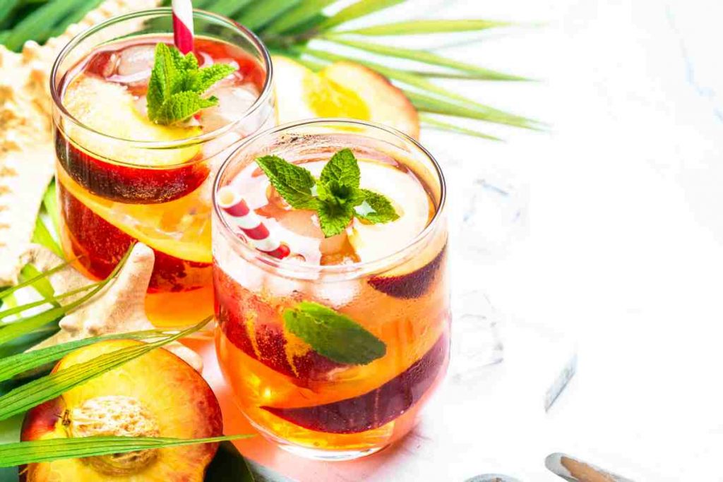 Spritz alle pesche in due bicchieri guarniti con foglie di menta