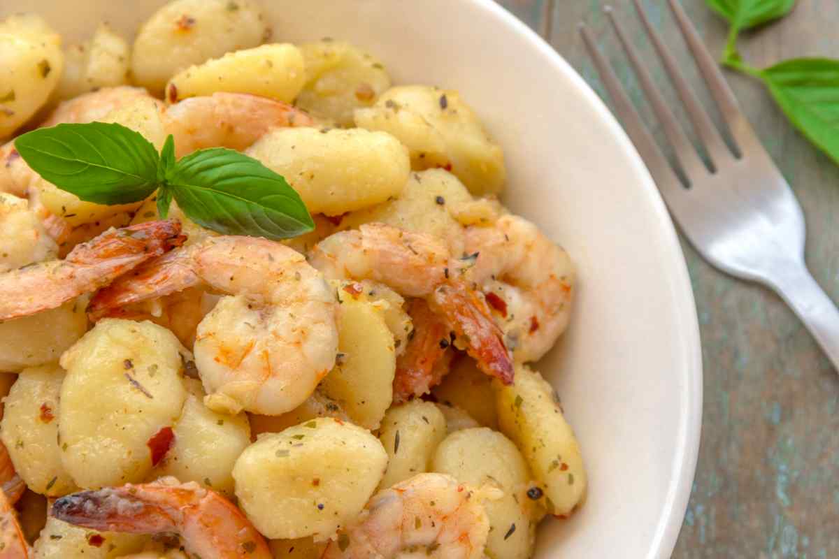 Gnocchi con i gamberi in un piatto bianco guarniti con foglie di basilico