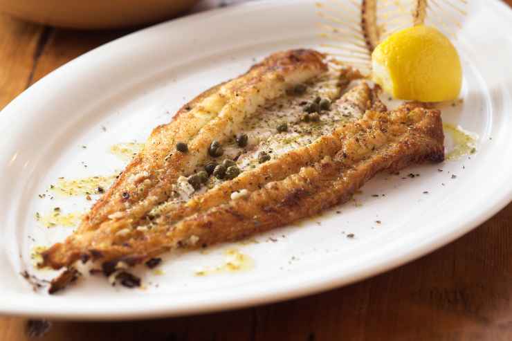 Sogliola con capperi in un piatto bianco con spicchio di limone