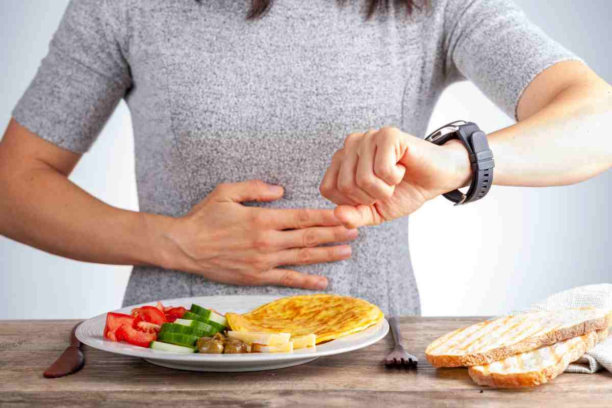 una donna guarda l'orologio con un piatto di cibo davanti come simbolo del digiuno intermittente