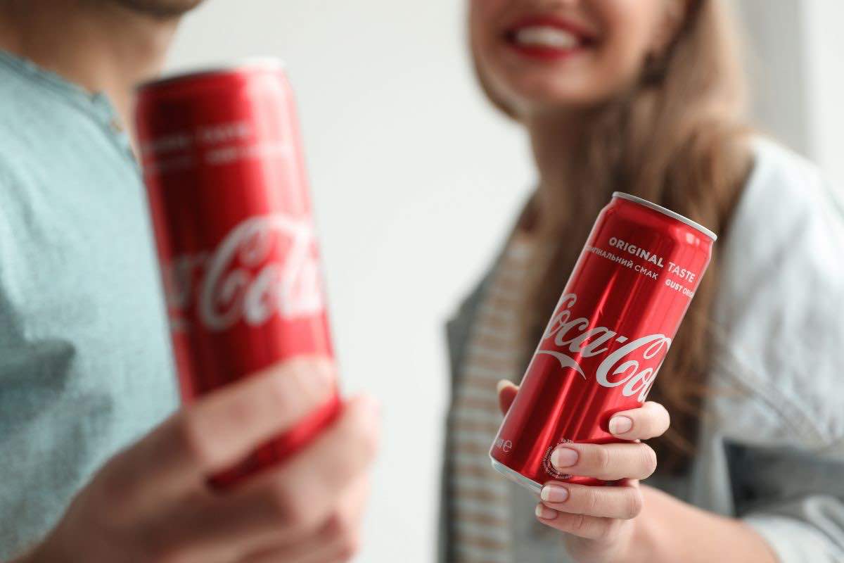 Due persone tengono in mano due lattine di Coca-Cola