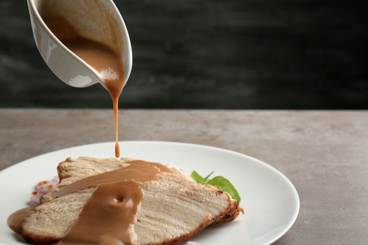 persona che versa salsa gravy sull'arrosto