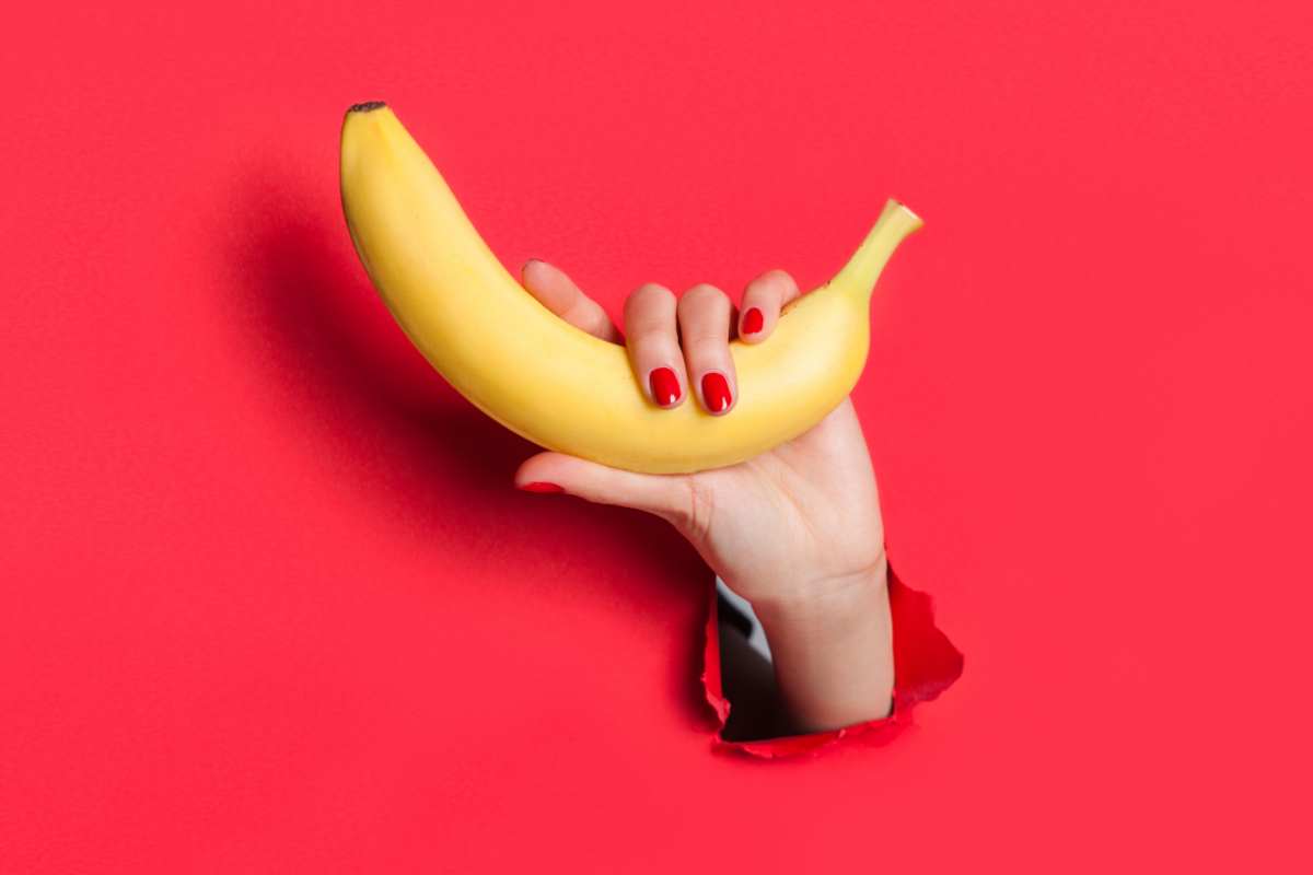 mano con banana su sfondo rosso