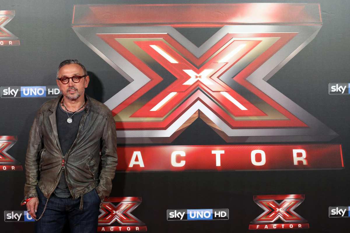 bruno barbieri sorride con dietro il cartellone di x factor