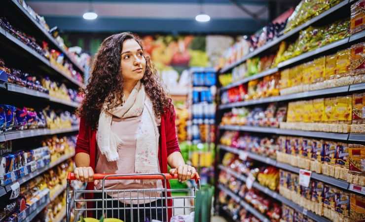 una ragazza in una corsia del supermercato col carrello