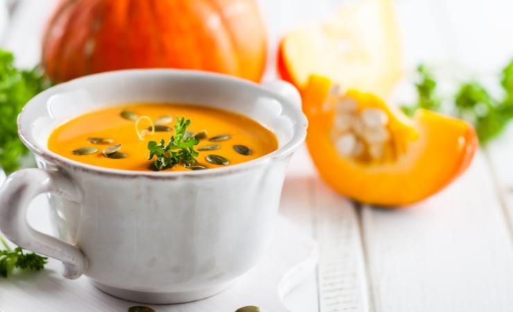 vellutata di zucca in tazza con zucca sullo sfondo