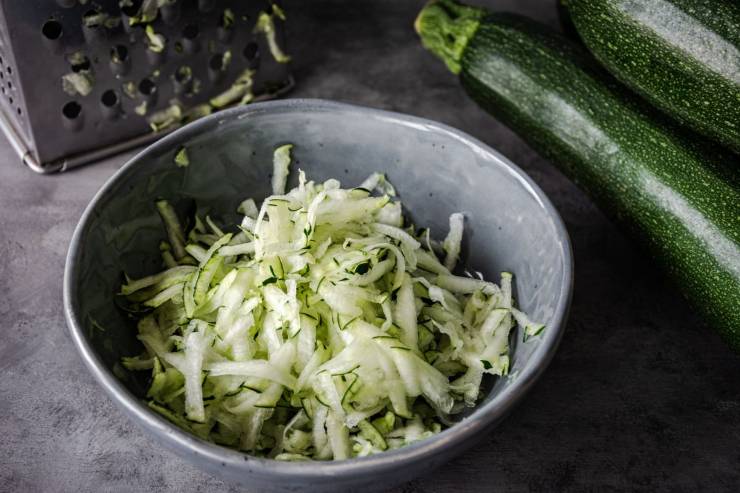 zucchine grattugiate in una ciotola e zucchine intere 