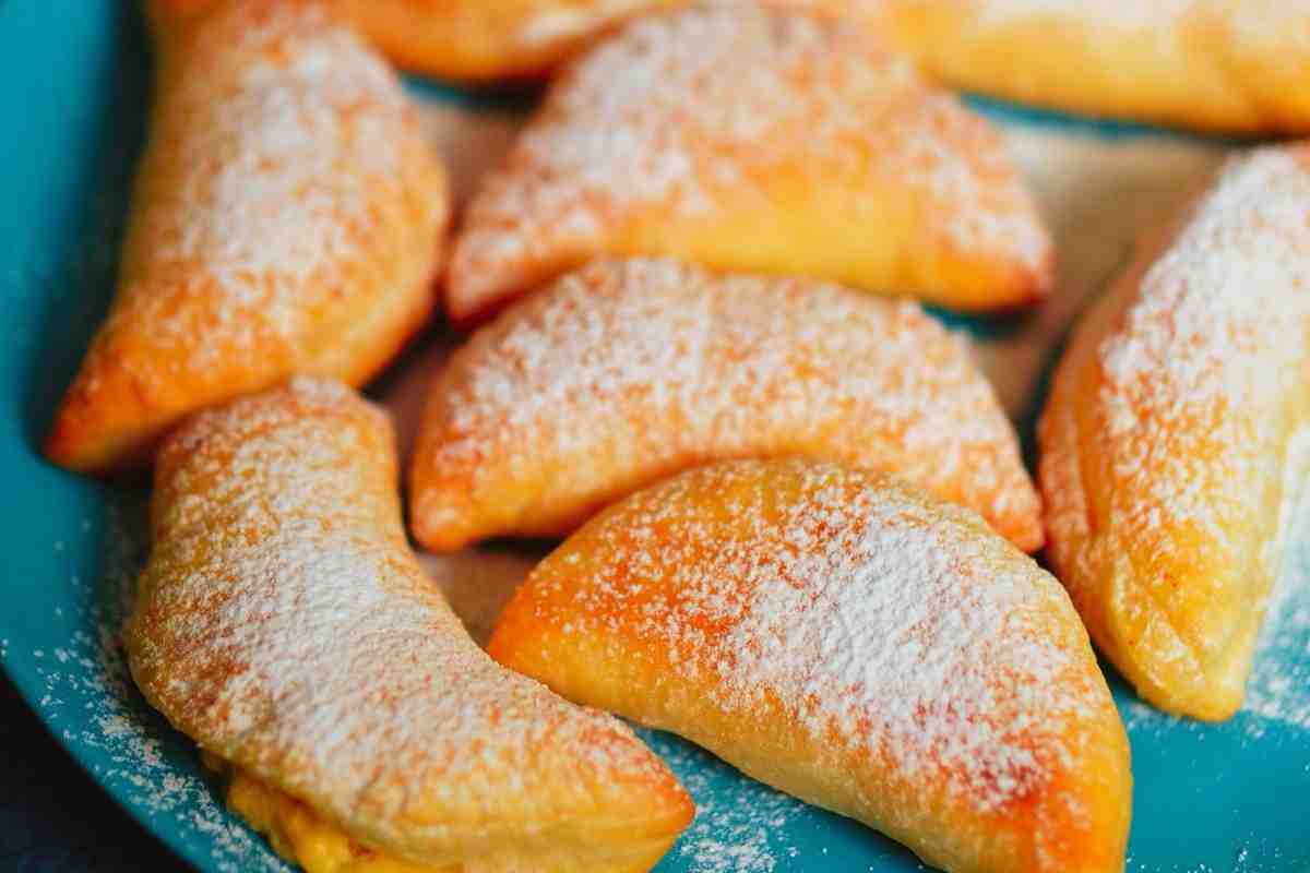 Ravioli di Carnevale a forma di mezzaluna spolverati di zucchero a velo su un piatto turchese