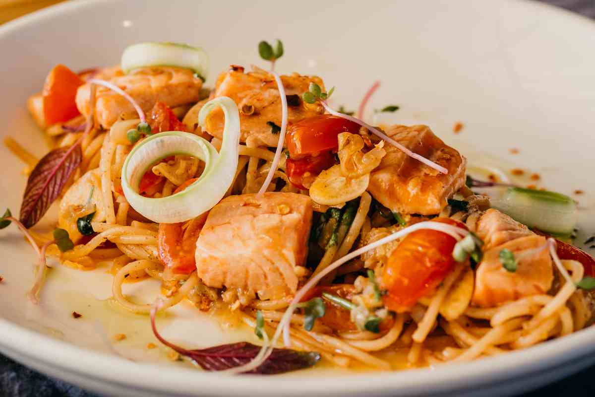 Spaghetti salmone e pomodorini in un piatto decorato con fiori eduli