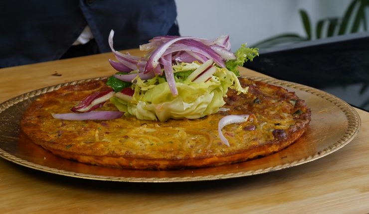 Frittata di pasta nel piatto con sopra insalata e cipolle 