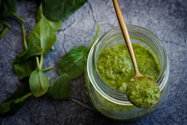 barattolo di pesto, cucchiaio, foglie di basilico