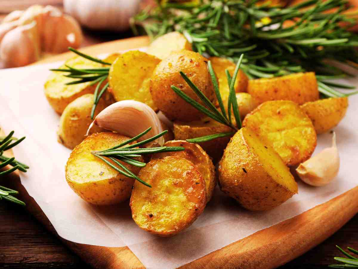 Patate novelle al forno con la buccia su un tagliere con foglie di rosmarino