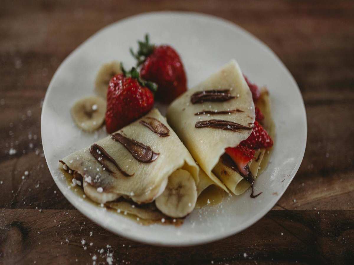 piatto con dentro due crepes farcite di frutta e ricoperte da crema spalmabile al cioccolato e accanto due fragole