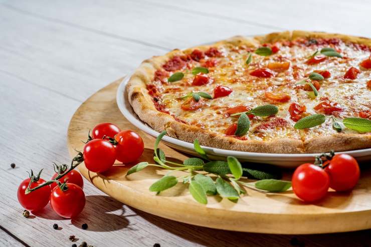 pizza con pomodorini su un tagliere di legno e accanto dei pomodorini