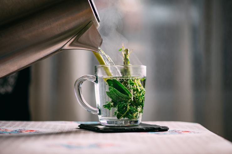 Versare l'acqua in un bicchiere con delle erbe